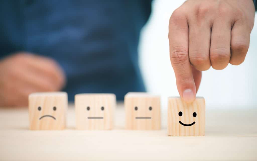 wood block cubes with different emotional faces, hand chooses smiling face