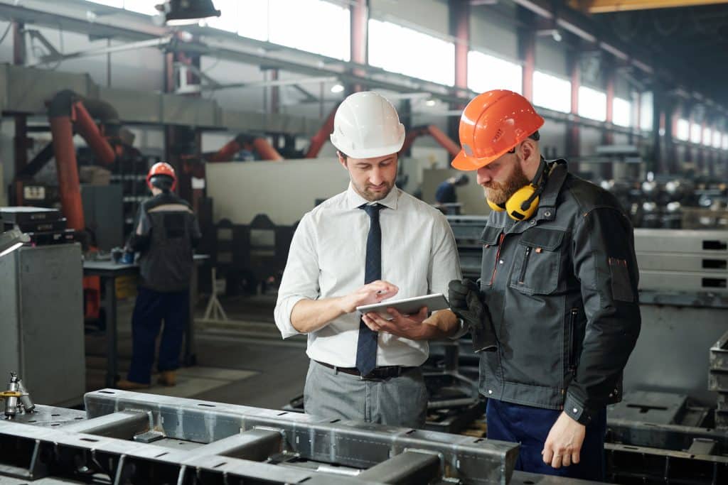 two man in hardhats looking at tablet in factory
